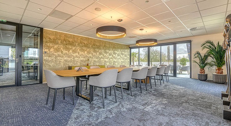 une vaste salle de réunion avec un papier peint jaune doré, une grande table et des sièges de travail