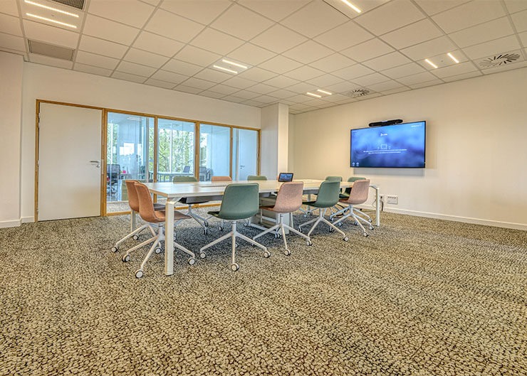 une salle de réunion avec une tables et des sièges sur roulettes et un écran de tv au mur